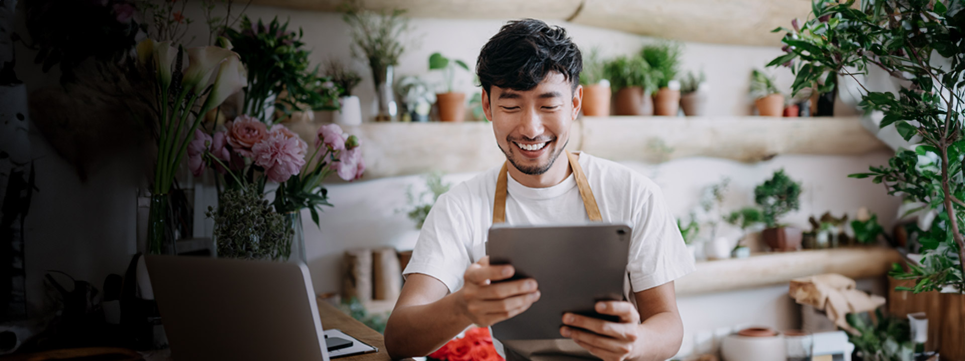 Flower shop owner smiling and looking at tablet.